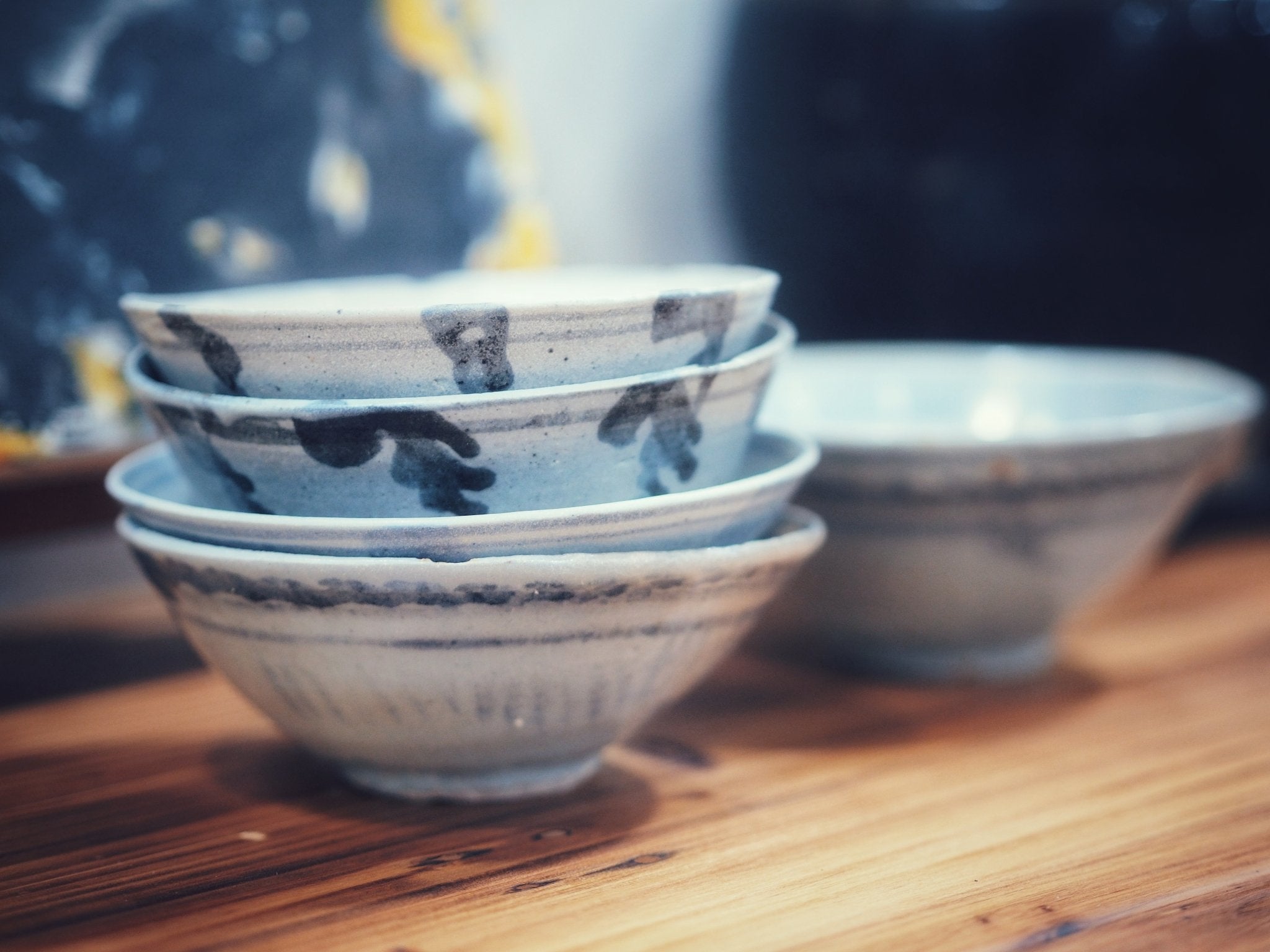 A stack of antique handcrafted ceramic tea bowls with rustic glaze patterns, displayed on a wooden table