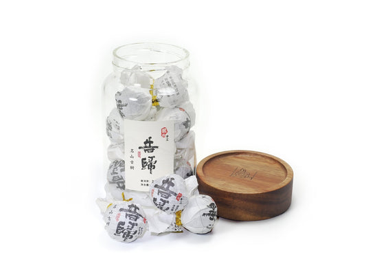 Opened jar of Xi Gui (昔归) Ancient Tree Raw Pu’er Tea with wooden lid beside it – individually wrapped tea balls displayed