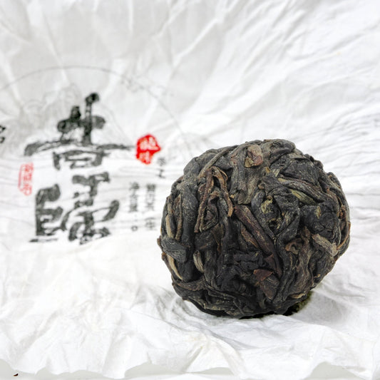 Close-up of unwrapped Xi Gui (昔归) Ancient Tree Raw Pu’er Tea ball showing dry leaf texture on traditional wrapper