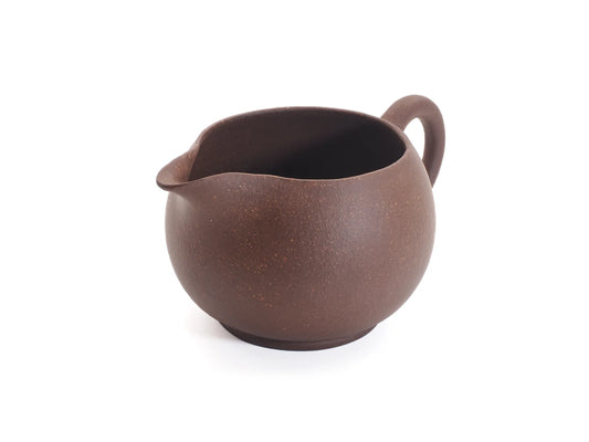Yixing zisha cha hai fairness pitcher in unglazed purple clay, three-quarter view showing the rounded pouring spout and ring handle